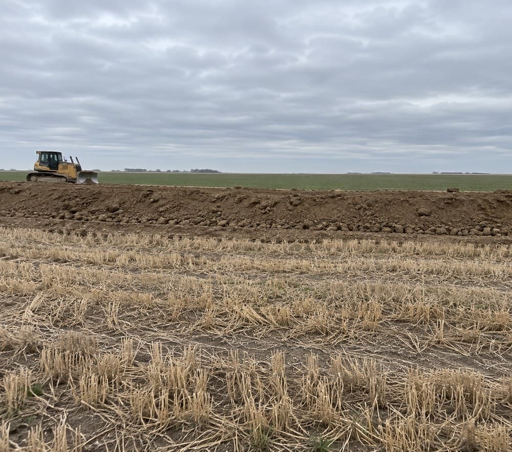 Graded open ground with equipment on the horizon, overcast